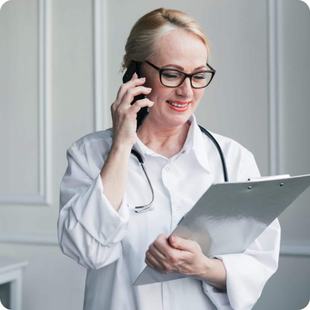 Smiling doctor speaking on the phone while holding a clipboard in a bright office