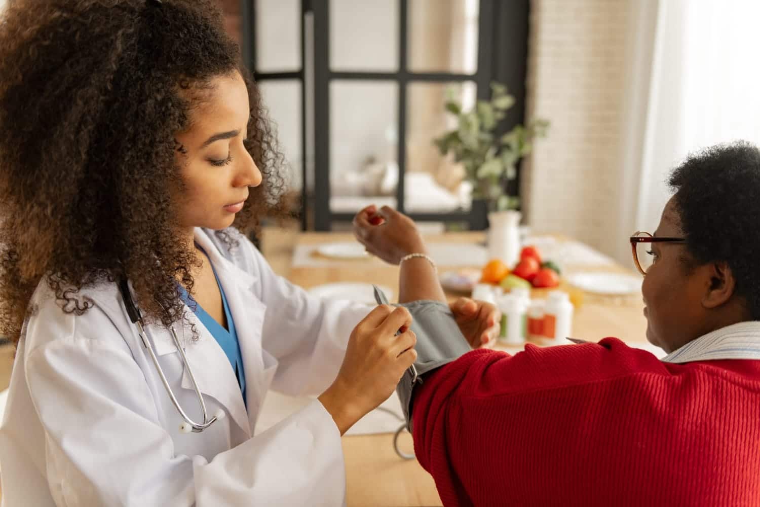 A healthcare provider checks a patient's blood pressure in a warm, home-like setting.