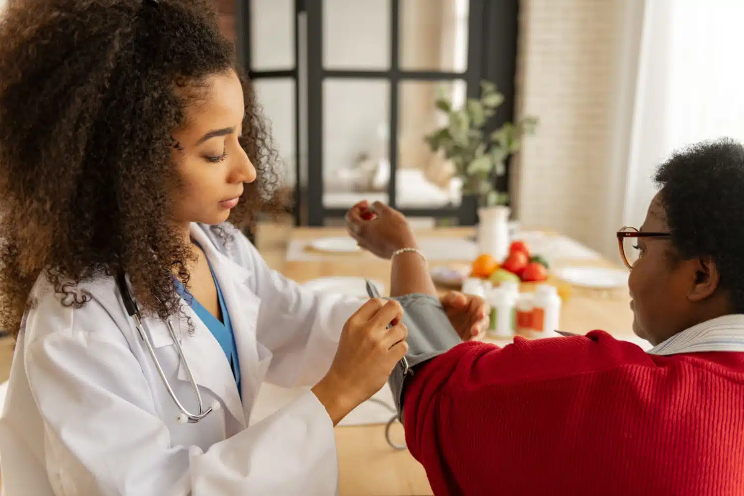 A healthcare provider checks a patient's blood pressure in a warm, home-like setting.